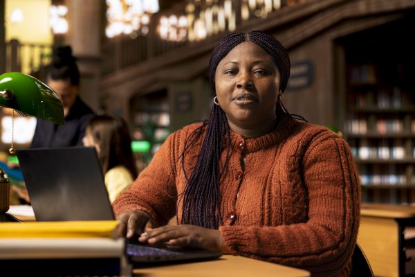 Portrait of african american librarian working with academic resources and learning materials within the public library database. Smiling woman focused on her educational profession.